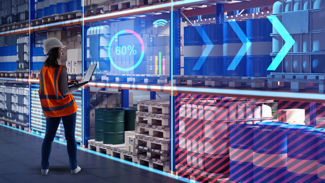 Female engineer in helmet and safety vest using laptop in smart warehouse with digital inventory management system and chemical barrels. - Smart logistics. Warehouse. Technology.