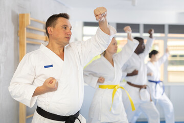 Group of multinational athletic people in kimonos try new fighting techniques at karate lessons