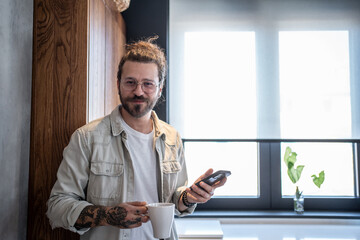 Freelancer enjoying morning coffee and checking smartphone in modern kitchen