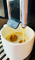 Espresso pouring from a coffee machine into a white cup