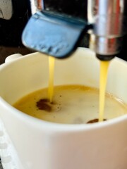 Espresso pouring from a coffee machine into a white cup