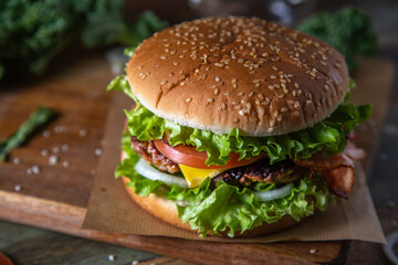 Homemade hamburger with cheese and herbs on a wooden cutting board