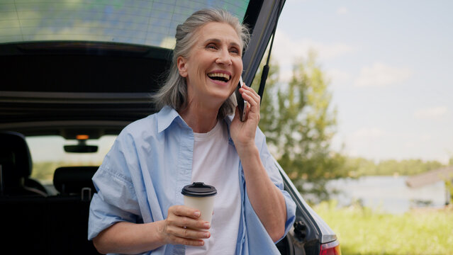 Happy smiling Caucasian retired business woman female senior mature automobile car driver businesswoman freelancer talking mobile phone speaking smartphone drinking coffee cup traveling outside nature