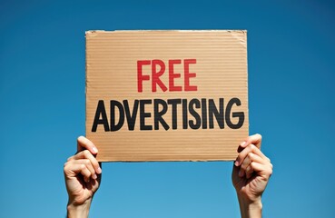 Hands hold cardboard sign with red text FREE and black text ADVERTISING against clear blue sky. This message board signifies business concept for promotion, public notice or announcement.