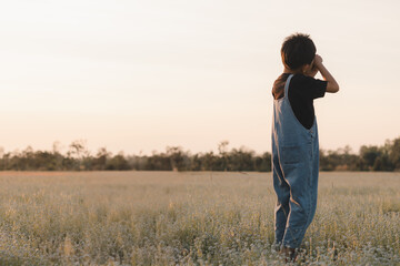 A young boy in overalls is standing in a flower field at sunset,  beauty of nature. His silhouette reflects joy, freedom, and the pursuit of dreams, perfect for themes of success and childhood play.