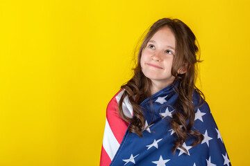 Portrait of young smiling cheerful caucasian girl wrapped with American USA flag on yellow...