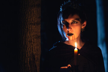 Vampire girl with dripping blood on her mouth and candle in the dark forest. Halloween theme.