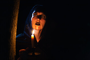 Vampire girl with dripping blood on her mouth and candle in the dark forest. Halloween theme.
