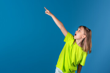 Cute european surprised teen girl pointing index finger to the left upwards side on blue...