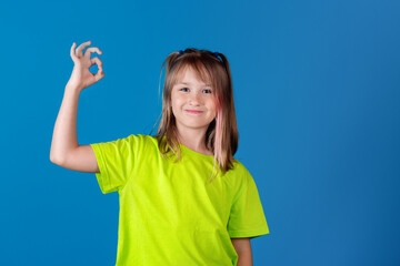 Young beautiful blonde european caucasian smiling girl showing OK sign against blue background