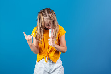 Cute european blonde girl with toy microphone singing and dancing against blue background. Rock...