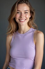 Fototapeta premium Portrait of happy young woman with wide smile. Wears casual lavender tank top, jeans. Blonde hair styled loosely. Studio setting with neutral background emphasizes features, cheerful expression,
