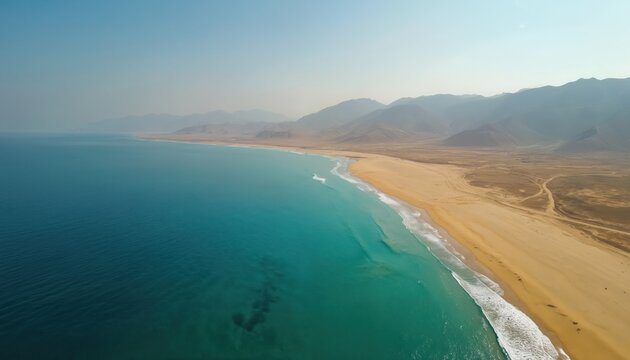 Aerial view of Balochistans Golden Beach, also known as Malan Beach, on Ras Malan coast. Turquoise ocean waves gently wash ashore sandy beach. Hazy mountains form backdrop. Clear sky suggests calm