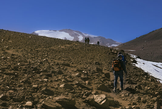Hikers ascending toward a snow-covered mountain under a clear blue sky