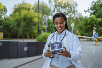 african american woman doctor walk with thermos and baby sonogram image
