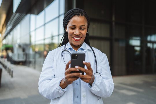 african american woman doctor on break use cellphone in front hospital