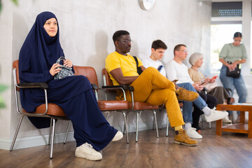 Girl in traditional veil, along with other people of different nationalities, is waiting for a...