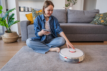Woman turns on smart vacuum cleaner to clean up the room. Smart home concept