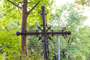 Ornate metal cross memorial monument standing among green trees in peaceful cemetery or memorial...