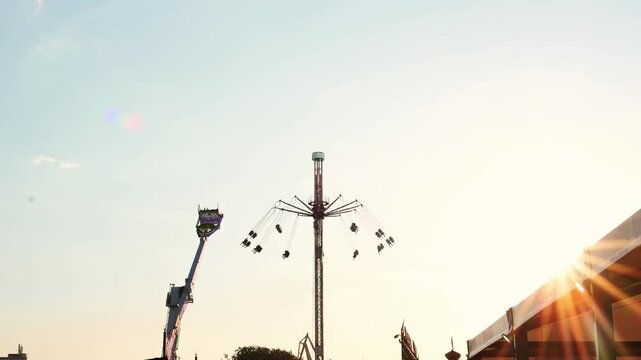 Rotating carousel swing ride spinning against warm sunset light, creating vibrant sun flare at bustling amusement park during golden evening hour