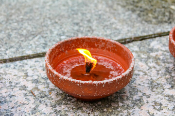 Single clay oil lamp with bright flame burning on textured stone surface