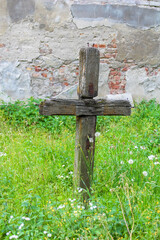 Simple wooden cross grave marker positioned in green grass against weathered brick wall creating humble memorial in historic cemetery