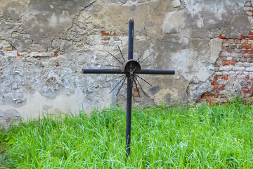 Tall metal cross memorial standing prominently against weathered brick wall in peaceful cemetery...