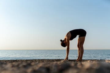 Fit woman doing morning yoga forward bend for health and flexibility by the sea