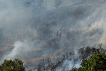 Forest fire engulfs mountainous terrain as firefighters battle flames amid thick smoke