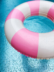 Swimming ring with pink and white stripes in a blue outdoor pool. Poolside atmosphere. Pink float.