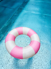 Swimming ring with pink and white stripes in a blue outdoor pool. Poolside atmosphere. Pink float.