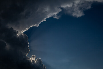 Dramatic sun sunbeams, break through bright, dark, white and blue clouds of thunderstorm 