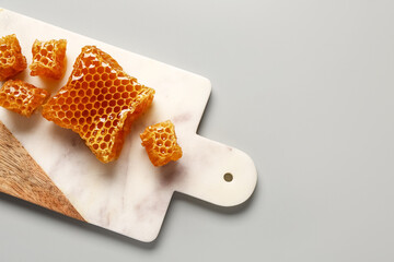 Board with sweet honeycombs on grey background