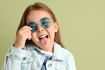 Cute little girl in sunglasses showing tongue on green background, closeup