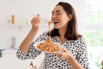 Young woman eating tasty pasta in kitchen
