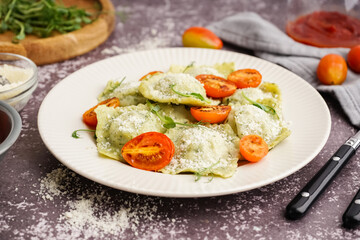 Plate of tasty ravioli with tomatoes and cheese on grey background
