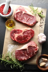 Pieces of raw beef meat and spices on black table, flat lay