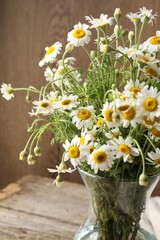 Beautiful chamomile flowers in glass vase on table, closeup