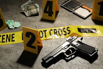 Forensic expertise. Crime scene with evidence, markers and police tape on grey background, closeup