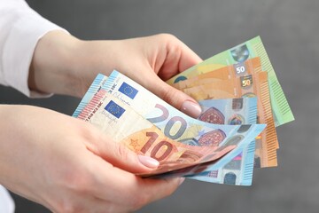 Woman counting euro banknotes on grey background, closeup