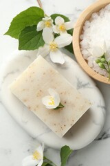Soap bar, sea salt and jasmine flowers on white marble table, flat lay