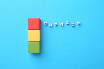 Colorful cubes and word Maximum made of beads with letters on light blue background, flat lay