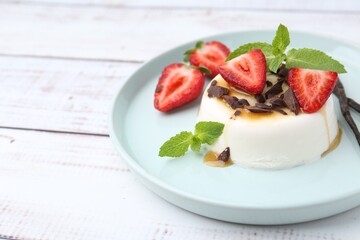 Tasty panna cotta with chocolate, strawberries, mint, caramel and vanilla pods on white wooden table, closeup. Space for text