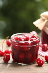 Tasty cherry jam and fresh fruits on wooden table against blurred background, closeup. Space for text