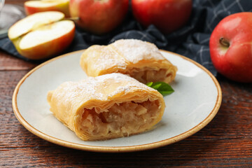 Pieces of tasty apple strudel with powdered sugar, mint and fruits on wooden table, closeup