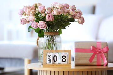 Calendar with date of International Women's Day, roses and gift box on table in bedroom, closeup
