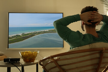 Young man watching travel show using video projector at home