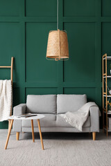 Interior of green living room with grey sofa, lamp, pillows and coffee table
