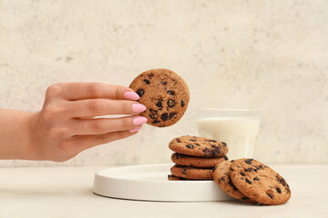 Female hand of sweet cookie with chocolate chips and glass of milk on white background