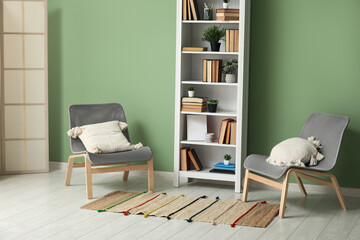 Bookcase with books and houseplants near cozy armchairs in living room